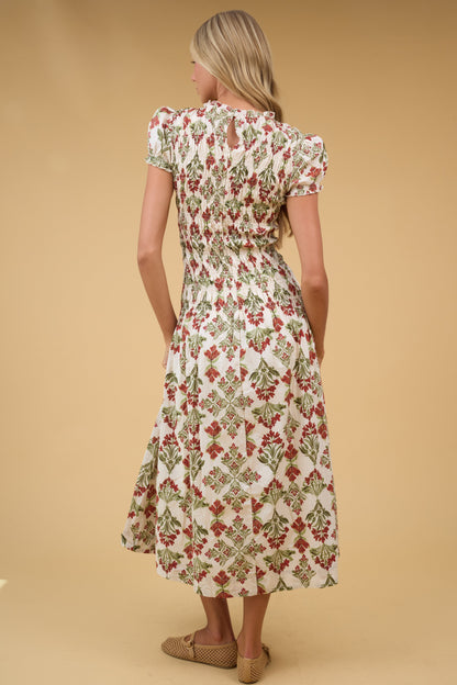 Back view of a woman wearing a cream floral midi dress with a smocked bodice and short puff sleeves.