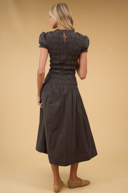 Back view of a woman wearing a back & brown gingham midi dress with short puff sleeves and smocked bodice.