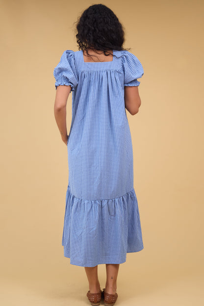 Back view of a woman wearing a loose fitting blue gingham midi dress with a square neckline.