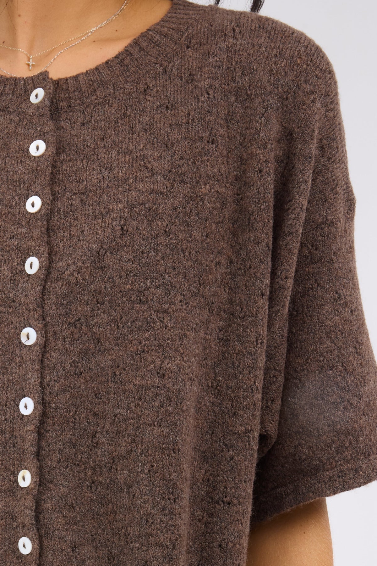 A close view of a woman wearing a brown pointelle knit, button down cardigan with short sleeves.