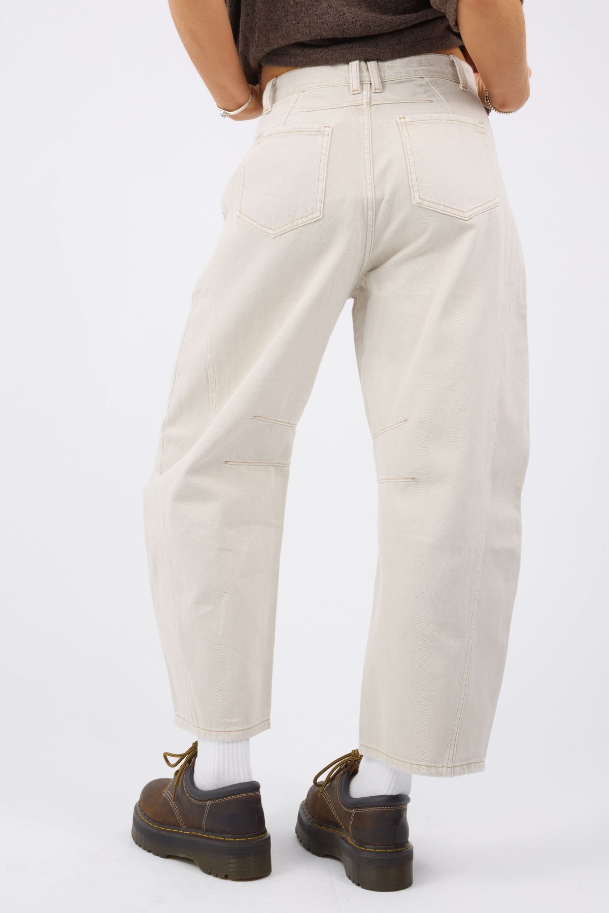 Back view of a youg woman wearing a pair of creamcolor barrel jeans with darts at the knees and back pockets.