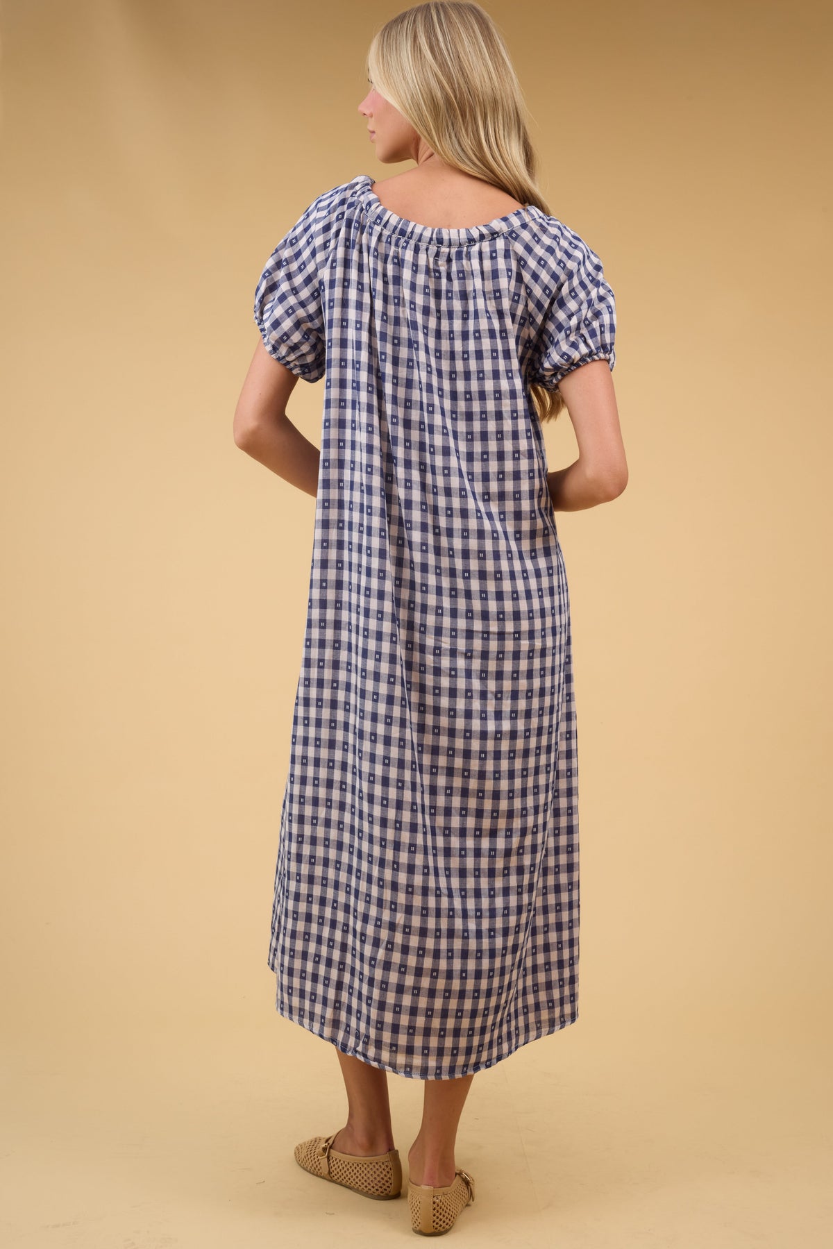 Back view of a young woman wearing a navy & cream gingham midi dress with large puff sleeves.