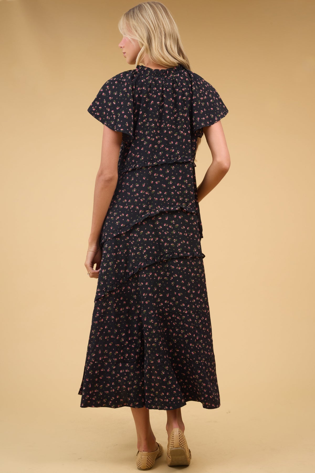 Back view of a woman wearing a  loose fitting black midi dres with narrow ruffle details and hort flutter fleeves.