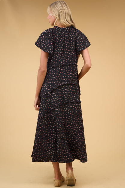 Back view of a woman wearing a  loose fitting black midi dres with narrow ruffle details and hort flutter fleeves.