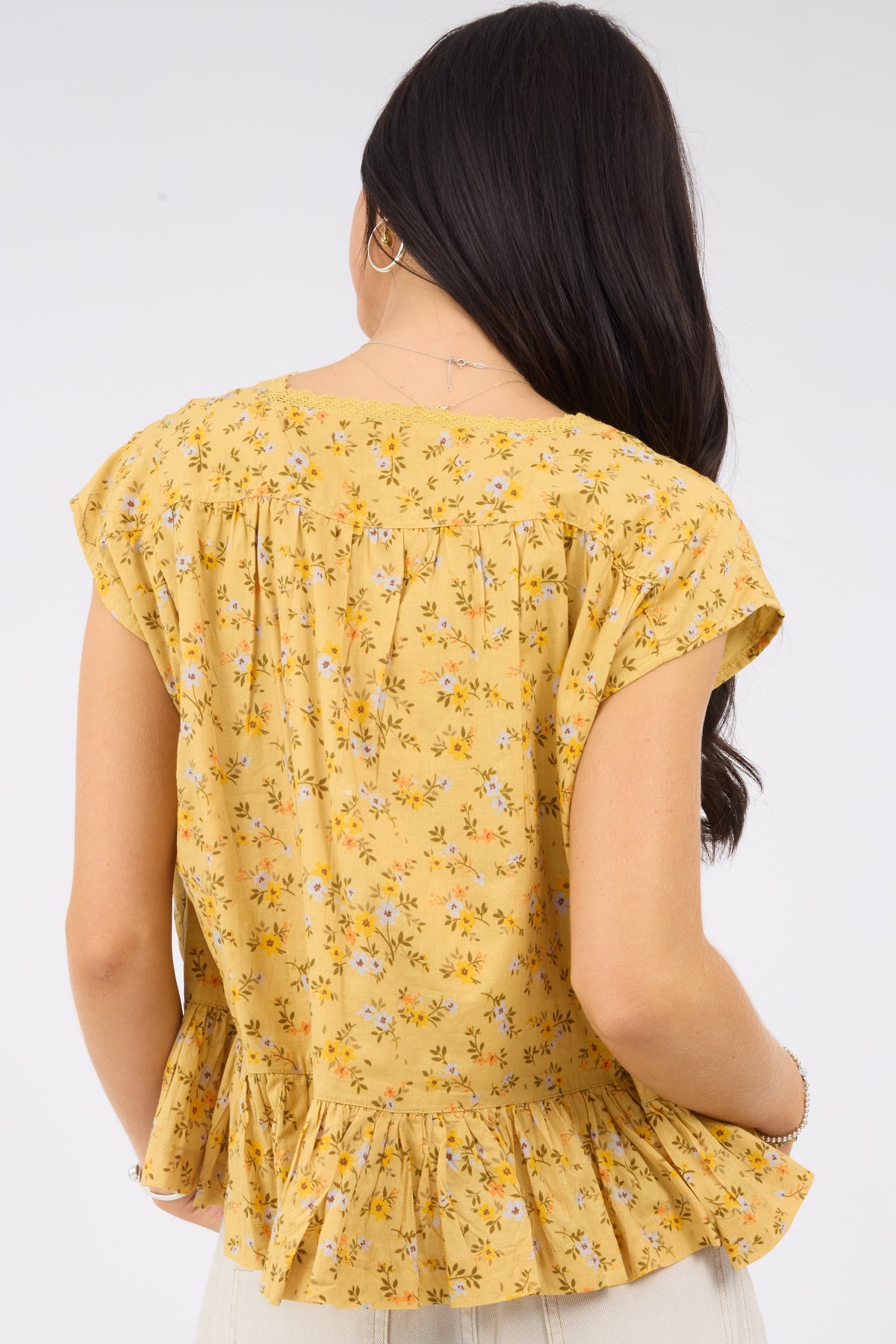 A back view of a woman wearing a yellow floral print blouse. 