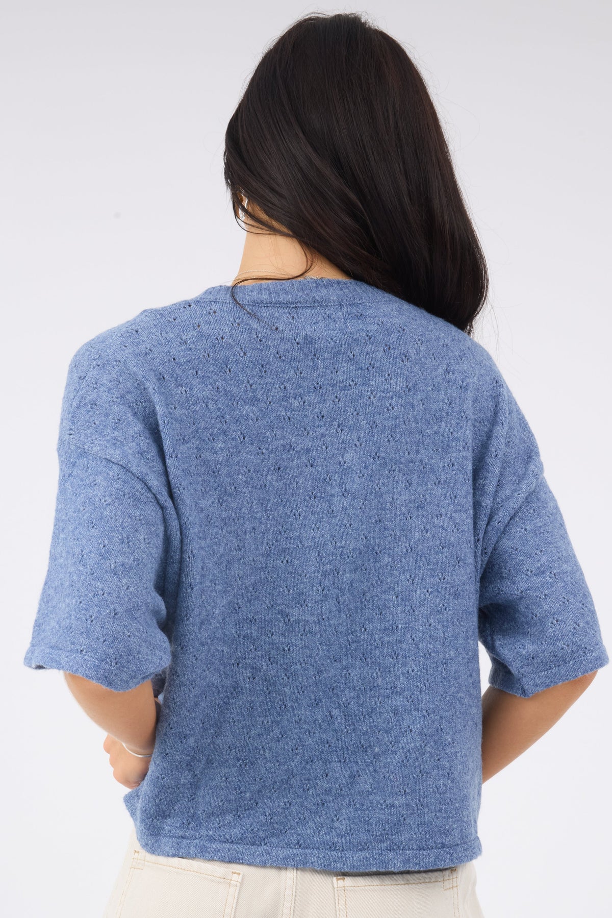 A back view of a woman wearing a blue pintelle knit sweater with short sleeves.