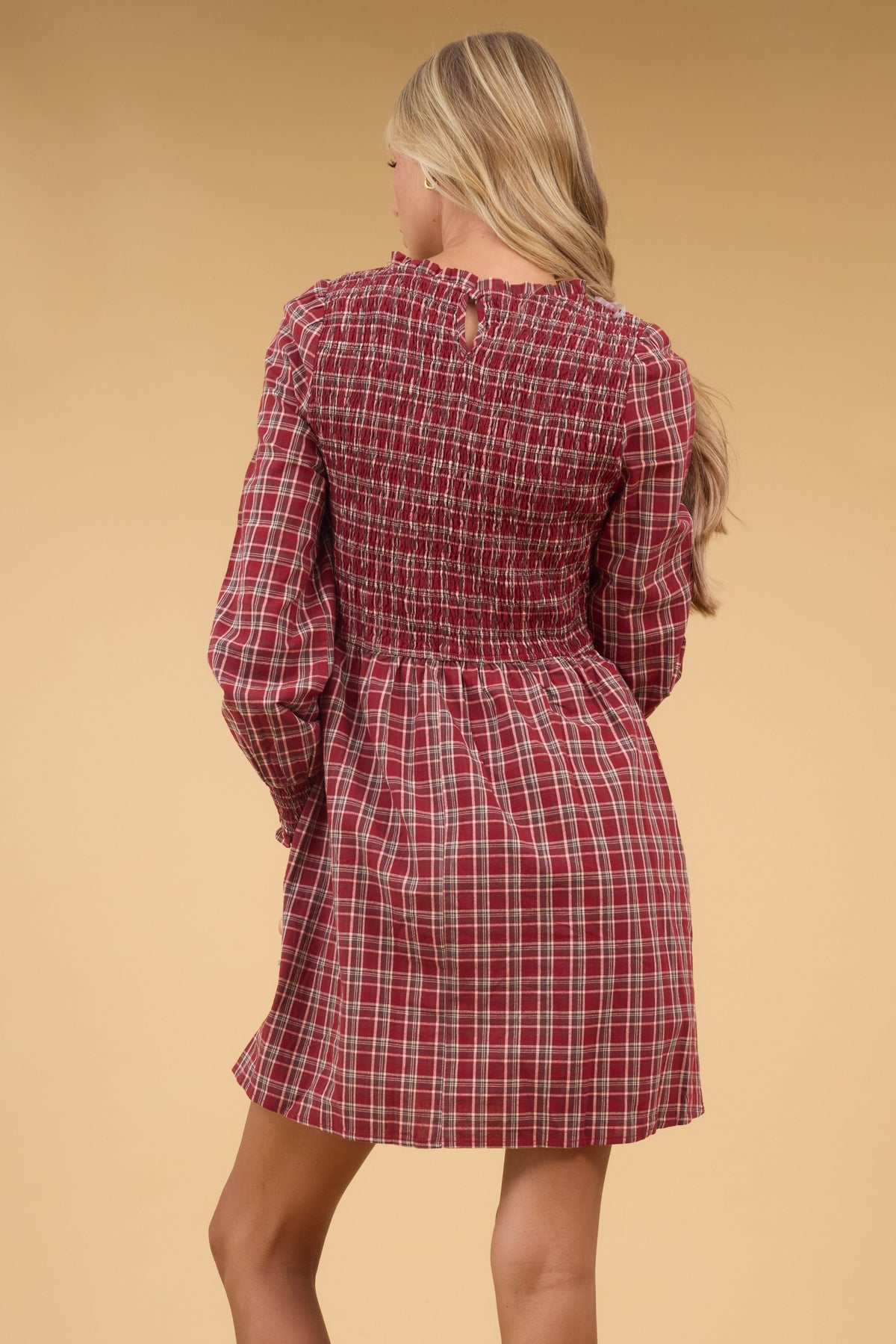 Back view of a woman wearing a red plaid dress with long sleeves and a smocked bodice.