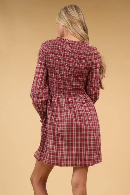 Back view of a woman wearing a red plaid dress with long sleeves and a smocked bodice.