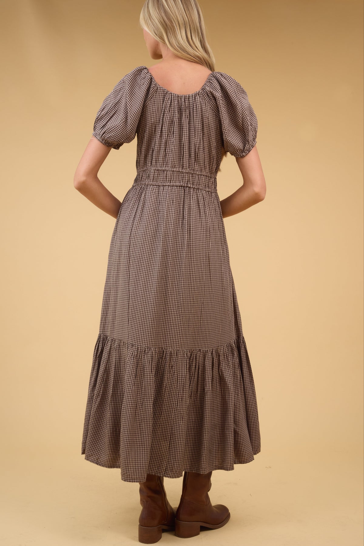Back view of a woman wearing a brown gingham midi dress with a wide bottom ruffle.