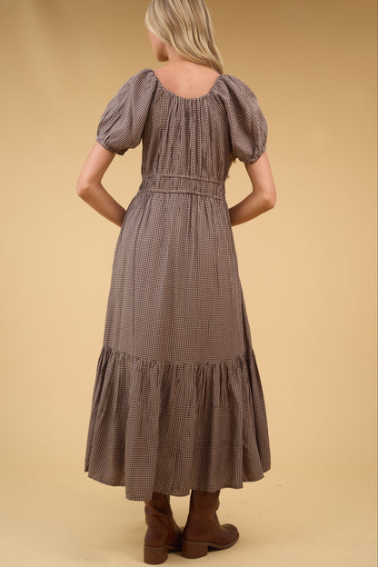 Back view of a woman wearing a brown gingham midi dress with a wide bottom ruffle.