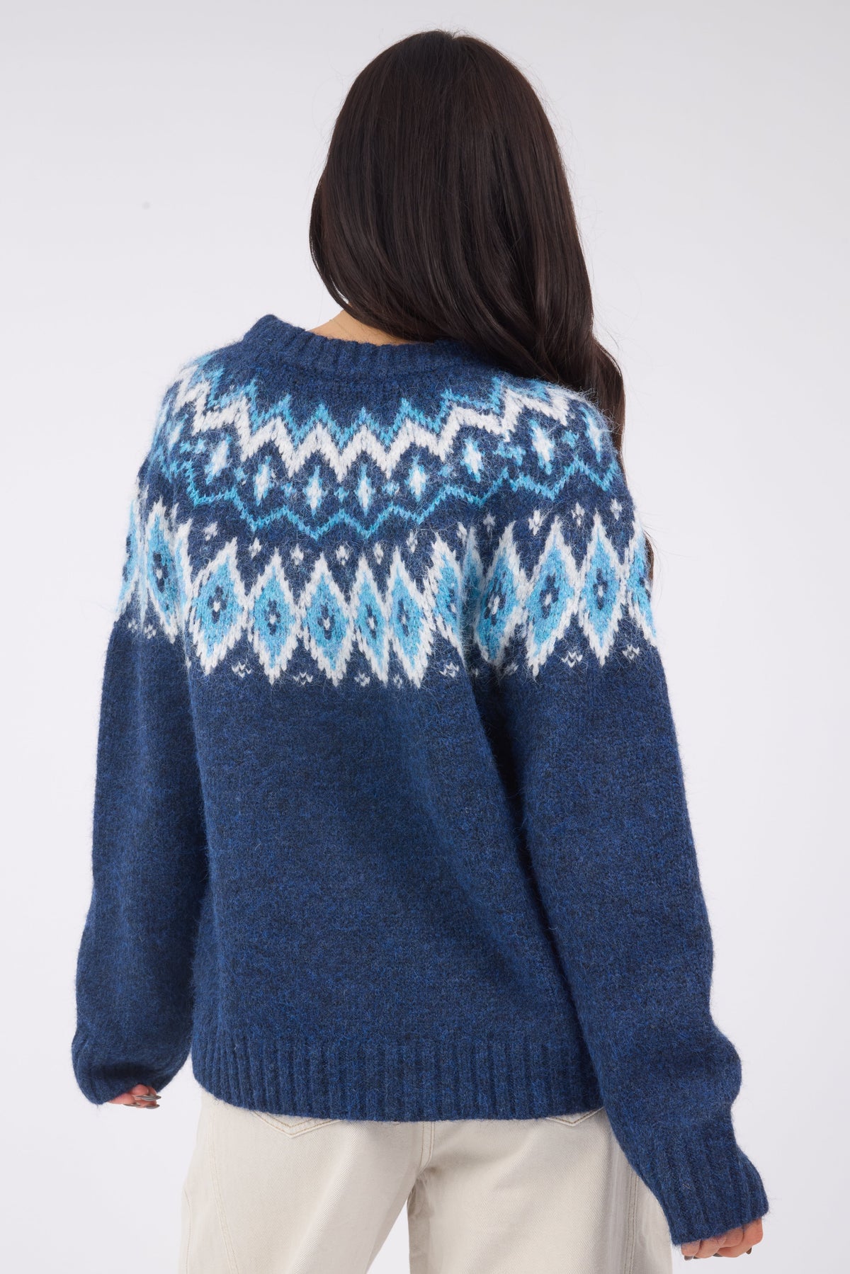 A back view of a young woman wearing a navy & blue nordic sweater with a wide crew neckline and long sleeves.