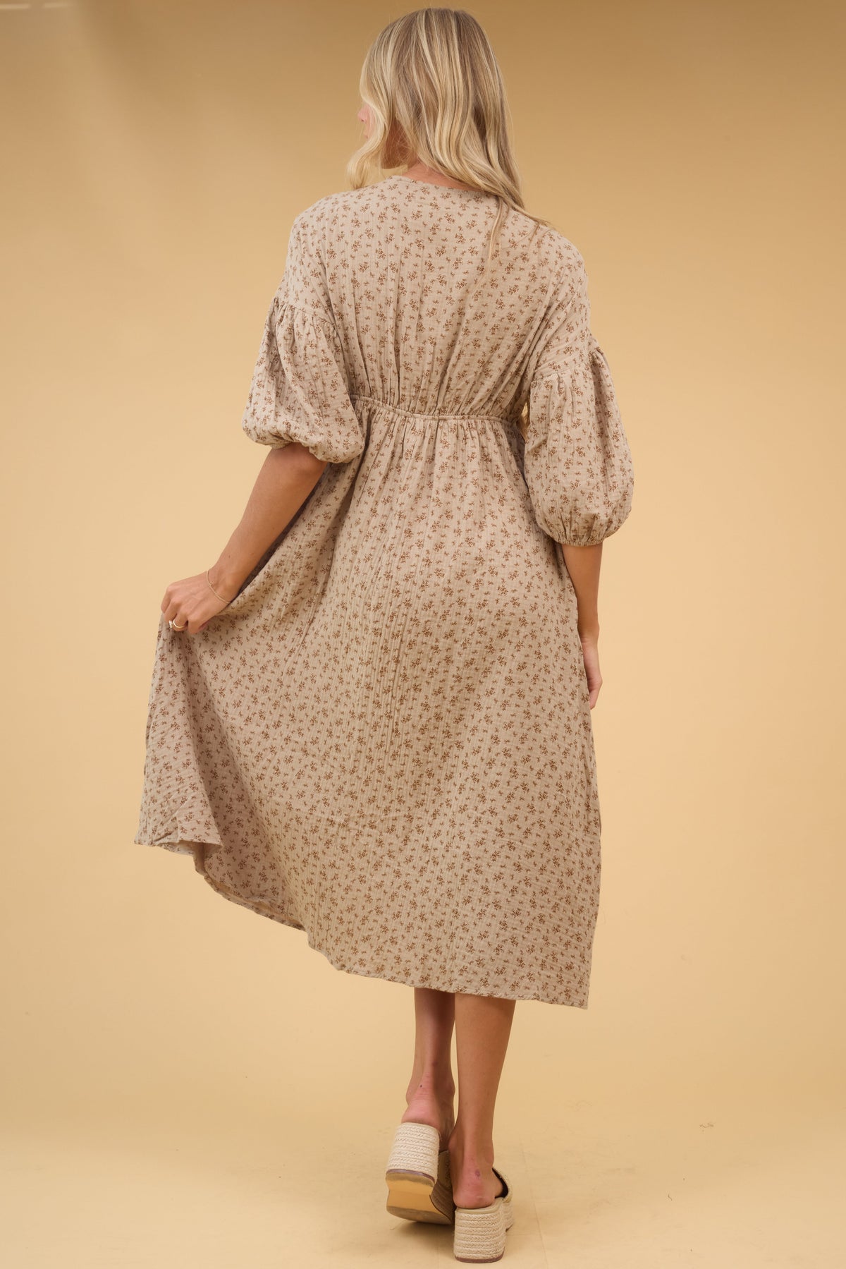 Back view of a woman wearing a tan floral midi dress with half length sleeves and back elastic waist.