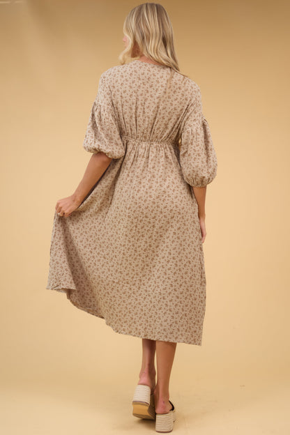 Back view of a woman wearing a tan floral midi dress with half length sleeves and back elastic waist.