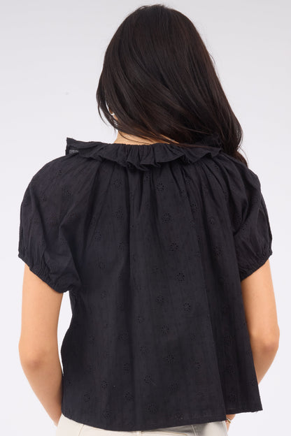 A back view of a young woman wearing a loose fitting black eyelet blouse with a ruffle neckline nad short puff sleeves.