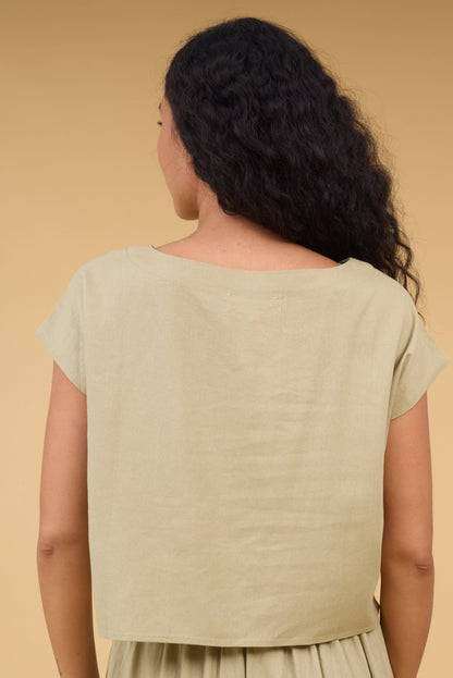 Back view of a woman wearing an olive loose fitting top with cap sleeves.