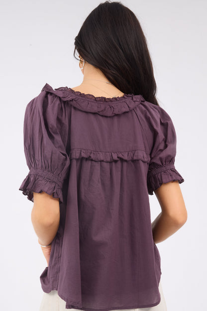 Back view of a woman wearing a loose fitting purple blouse with ruffle details.
