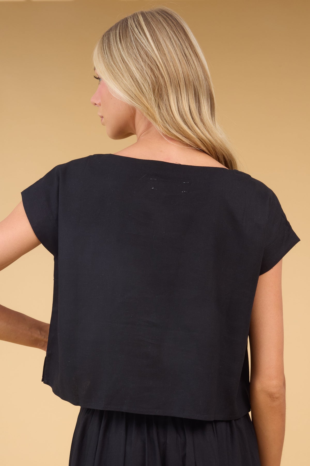 Back view of a young woman wearing a loose fitting cap sleeve blouse in black.