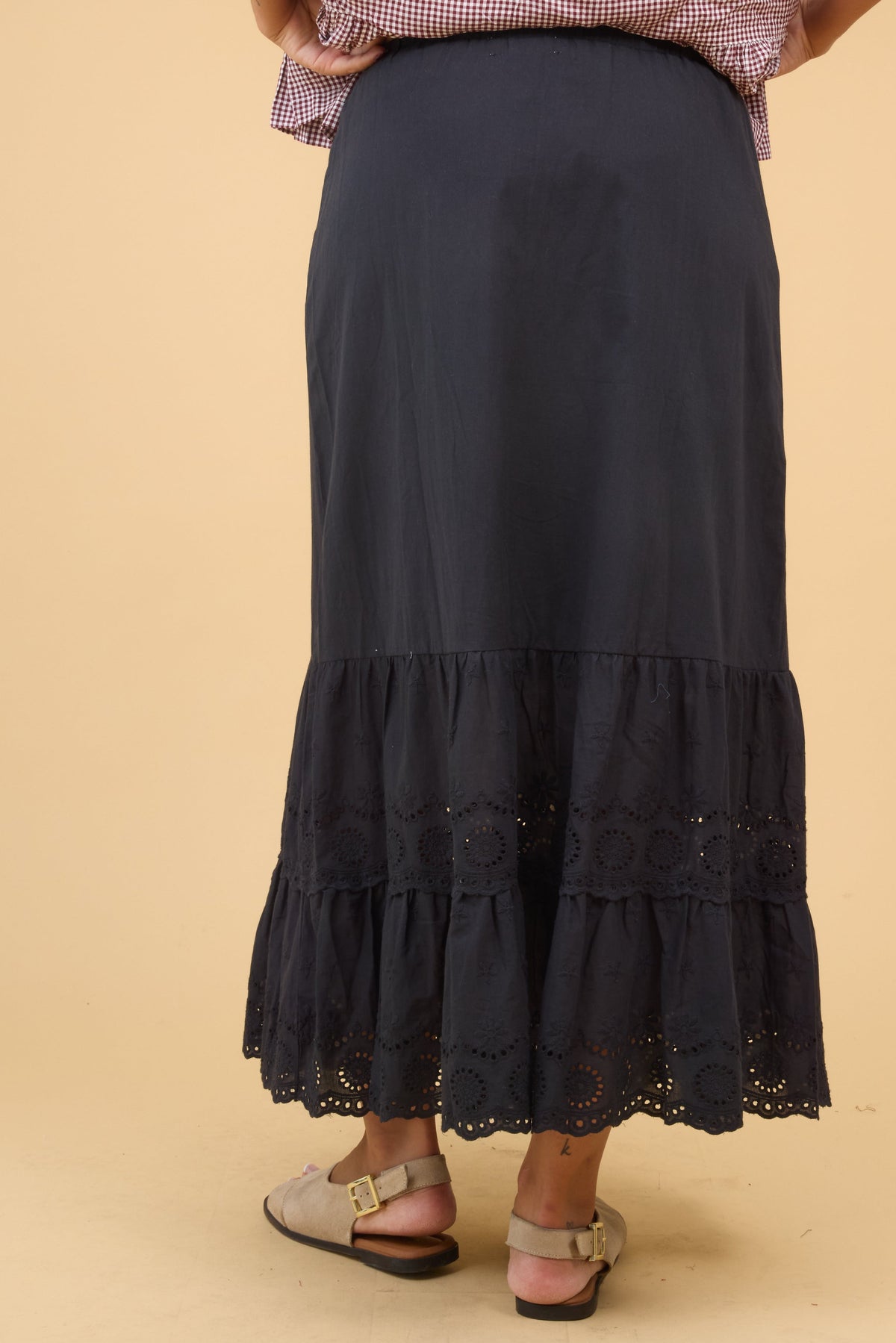 Back view of a woman wearing a black midi skirt with a wide eyelet ruffle.