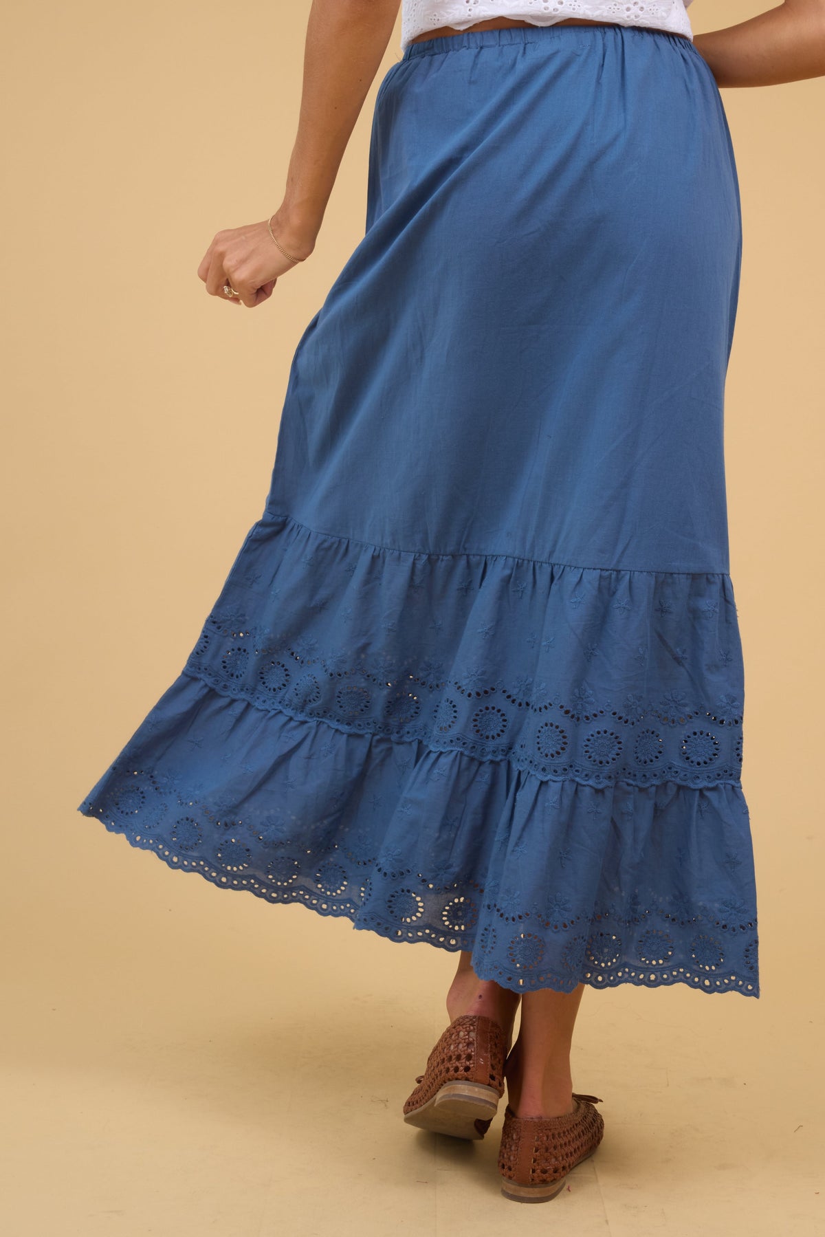 Back view of a woman wearing a blue midi skirt with a double eyelet ruffle.