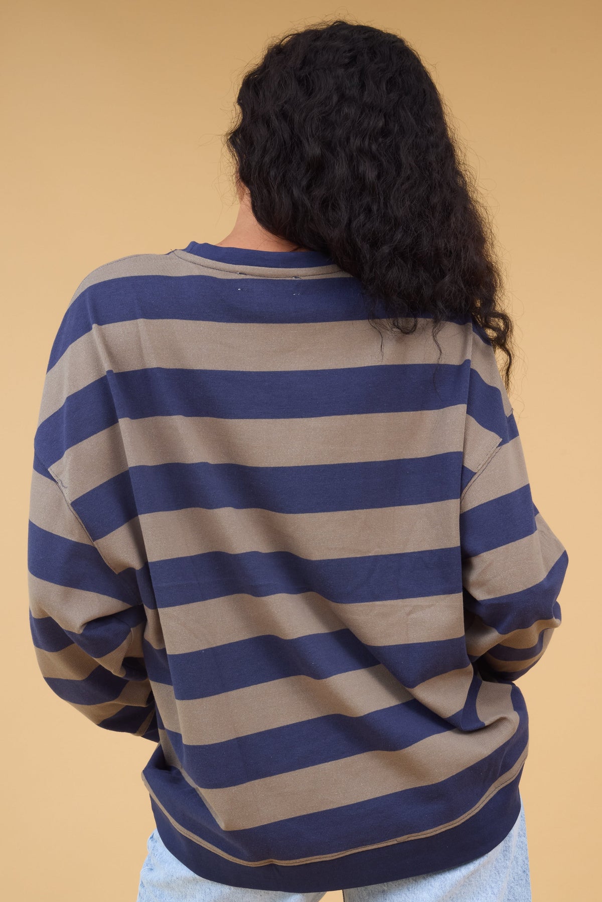 Back view of a woman wearing a taupe & navy stripe top with long sleeves.