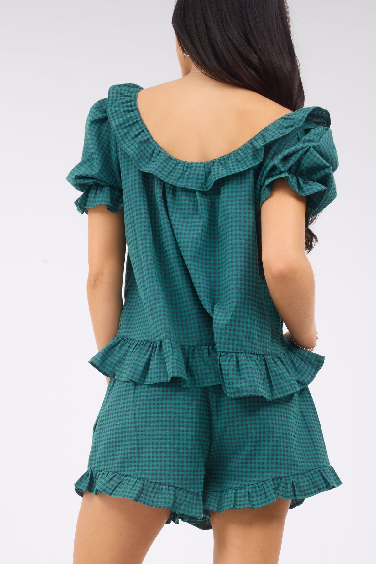 Back view of a woman wearing a green & navy gingham short set with a wide ruffled neckline, short puff sleeves and ruffled hems.