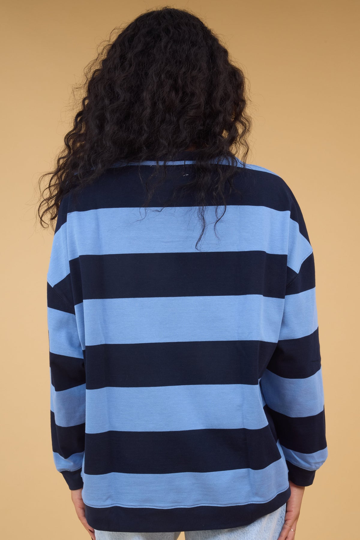 Back view of a woman wearing a light blue & navy wide stripe top with long sleeves.