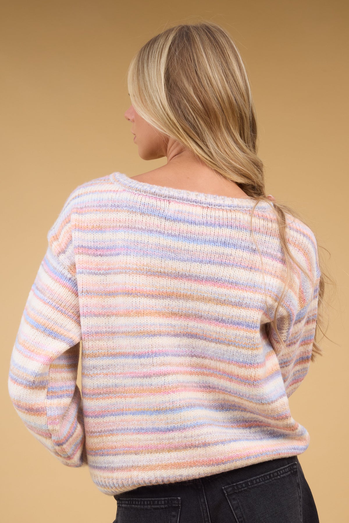 Back view of a woman wearing a muted rainbow stripe pullover sweater with long sleeves.