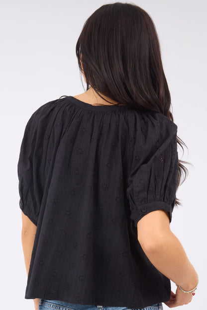 A back view of a woman wearing a black eyelet blouse with short puff sleeves.