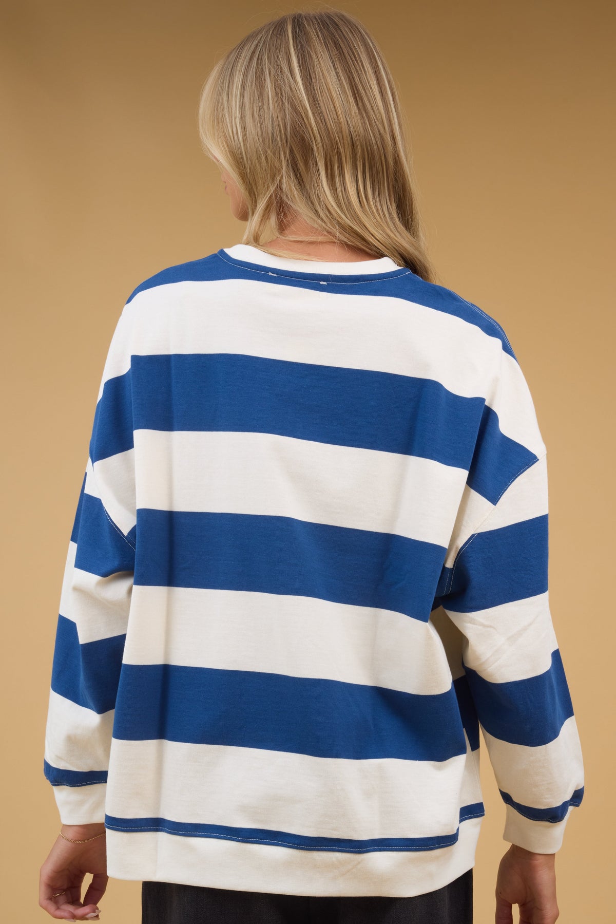Back view of a woman wearing a blue & cream wide strip top with long sleeves.