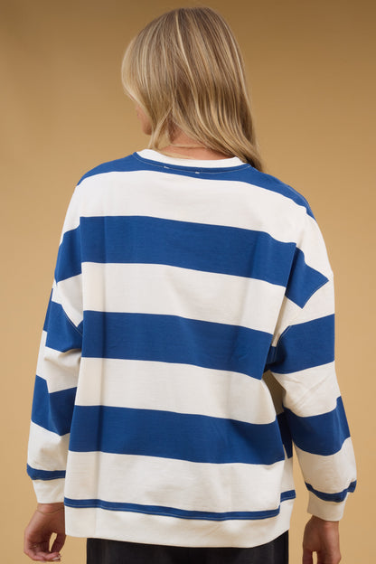 Back view of a woman wearing a blue & cream wide strip top with long sleeves.