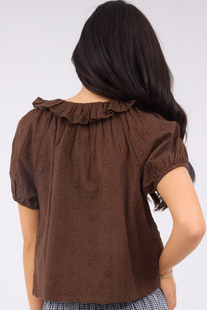 A back view of a woman wearing a brown eyelet blouse with shrot puff sleeves and a ruffled neckine.