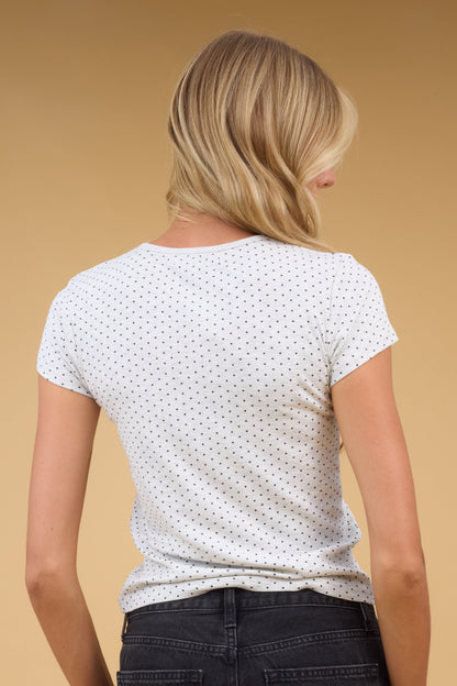 Back view of a woman wearing a  light grey knit tee with tiny black polka dots and short sleeves.