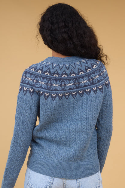 Back view of a woman wearing a blue cable knit sweater with a nordic patter yoke.