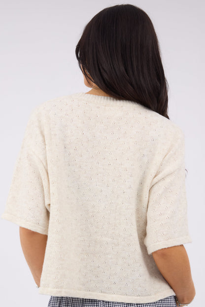 A back view of a woman wearing an oatmeal short sleeve sweater in a pointelle knit.