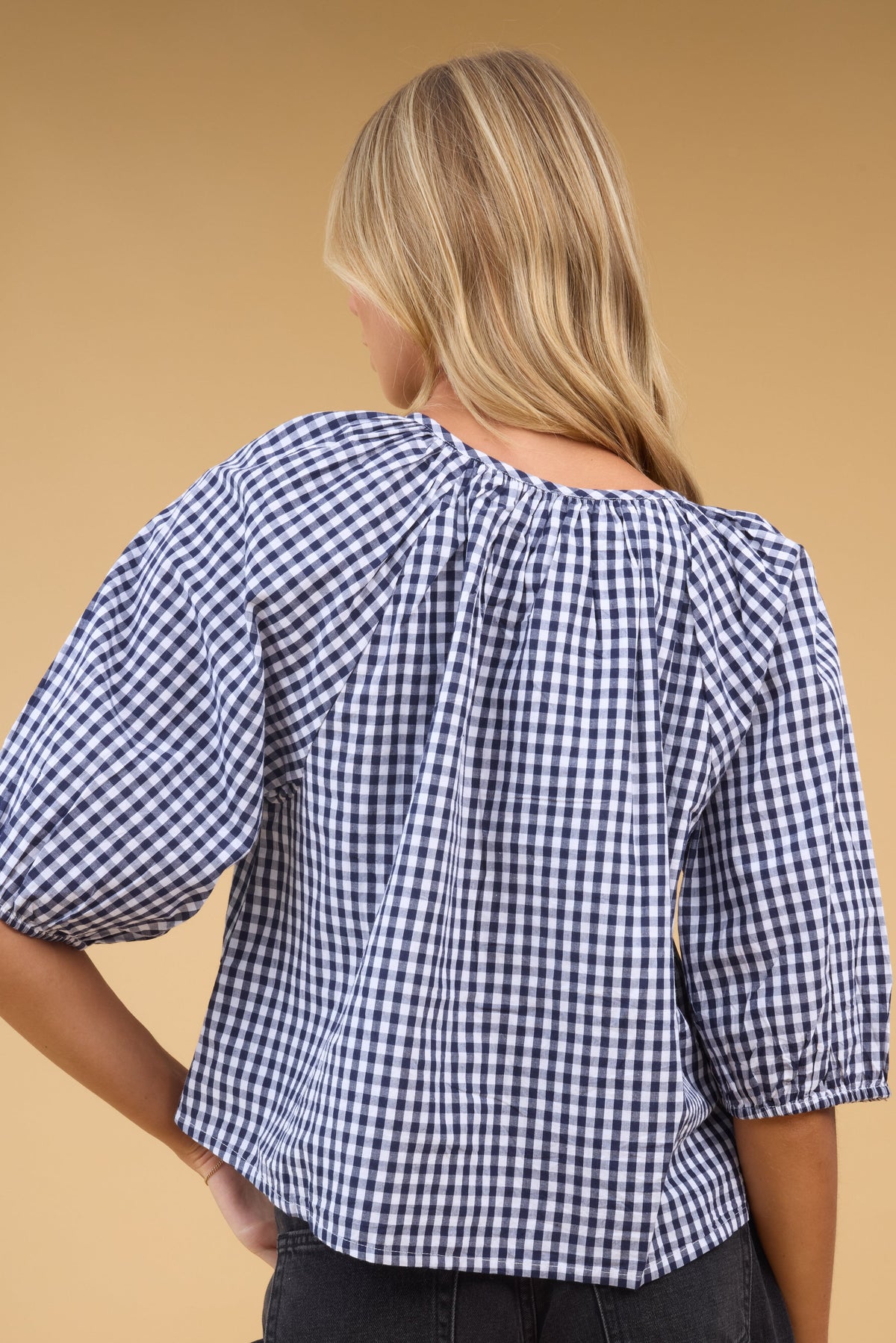 Back view of a woman wearing a avy & white gingahm blouse with half length sleeves.
