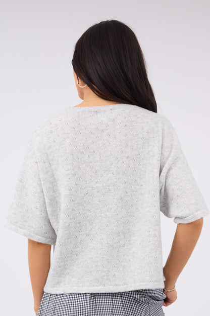 Back view of a woman wearing a loose fitting pointelle knit sweater in a light grey 