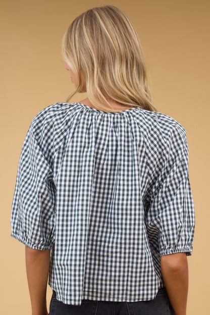Back view of a woman wearing a loose fitting green gingham blouse with half length sleeves.