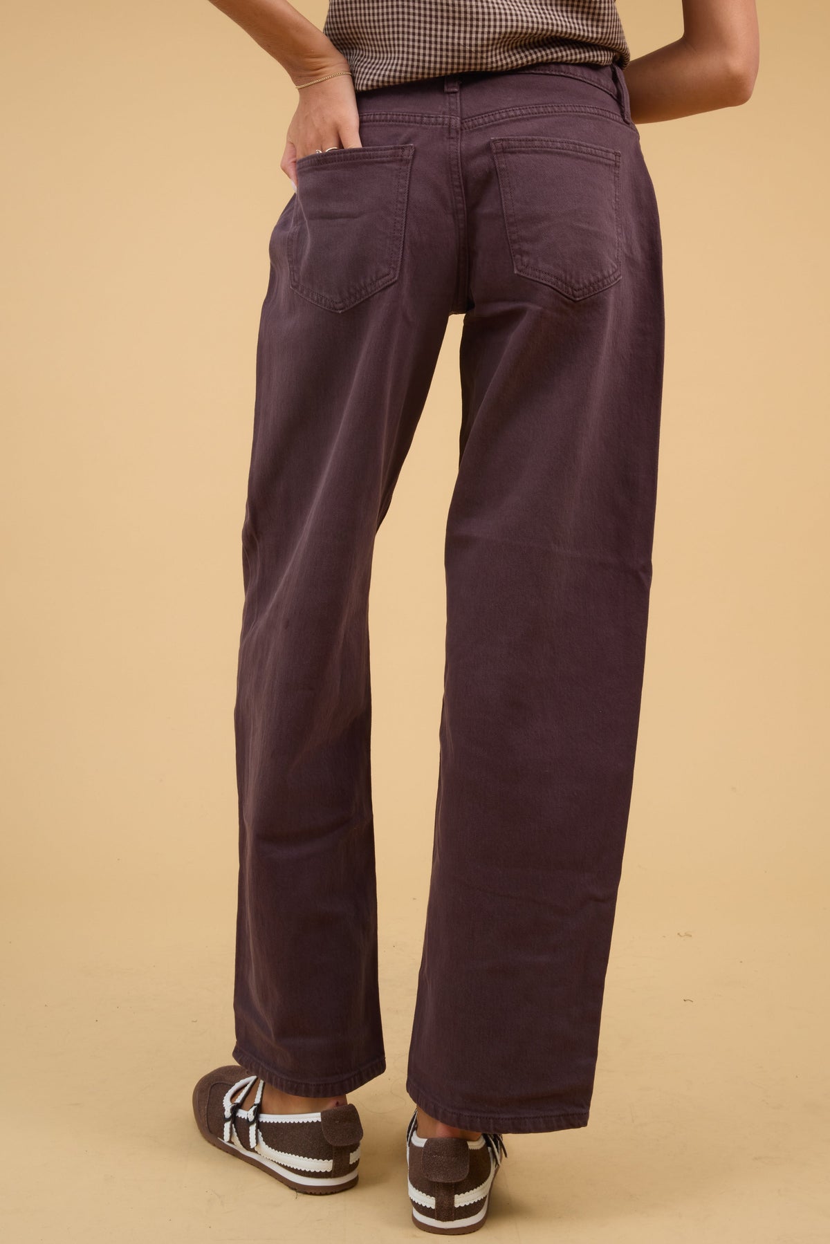 Back view of a young woman wearing a pair of brown wide leg jeans with back patch pockets.