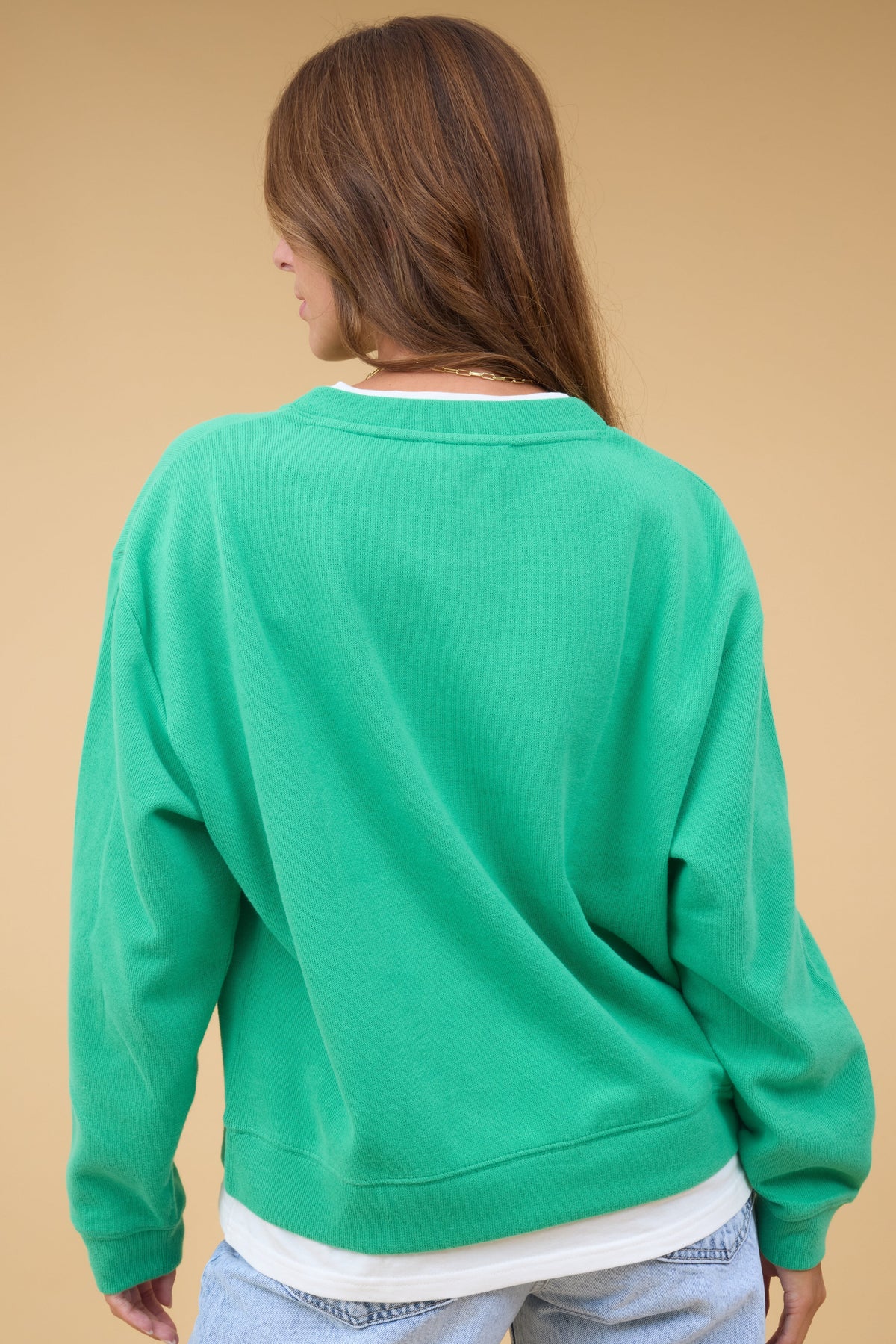 Back view of a woman wearing a loose fitting green sweatshirt with faux white tee details.