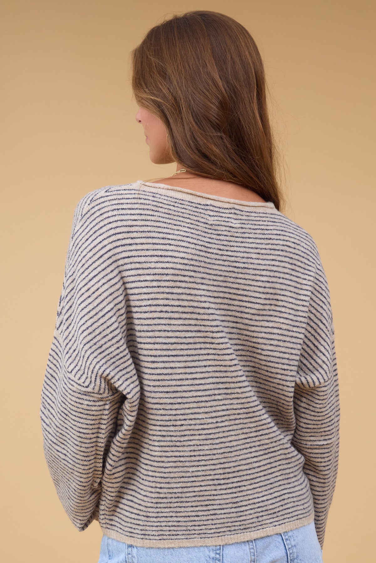A back view of a woman wearing a loose fitting natural & black stripe sweater with long sleeves.
