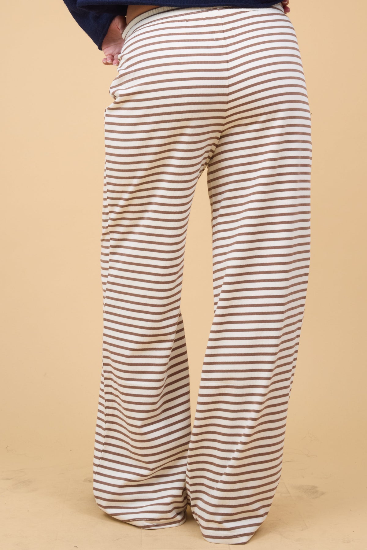 Back view of a young woman wearing a pair of wide leg crewm & brown stripe lounge pants.