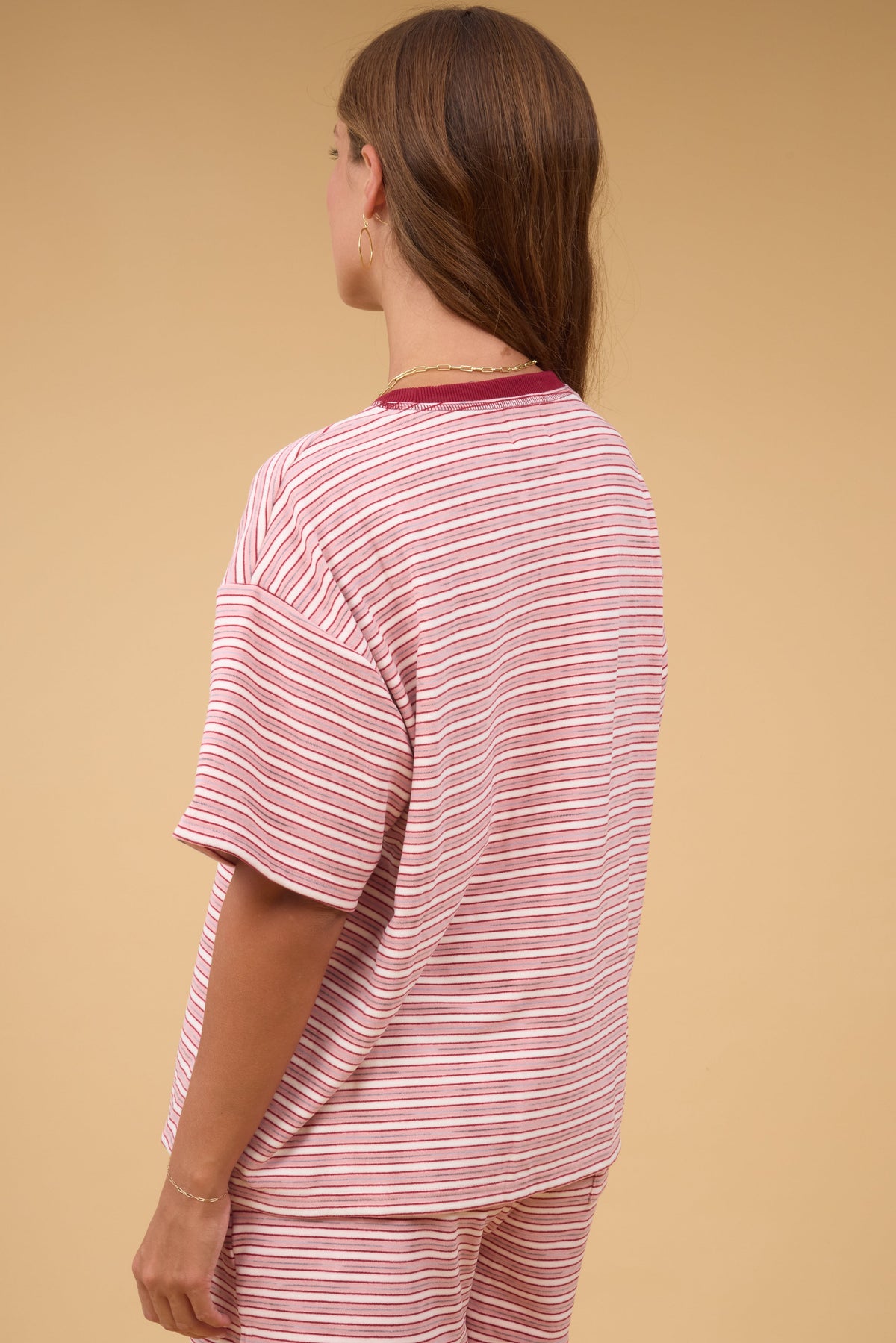 Back view of a woman wearing a oft pink & white stripe loose fitting top with short sleeves.