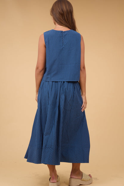 A back view of a young woman wearing a loose fiting skirt  and blouse set in navy & black plaid.