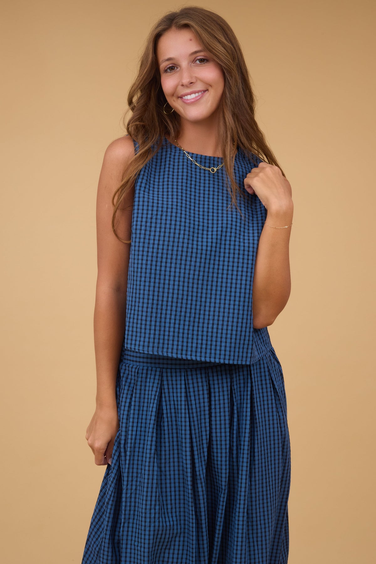 A young woman wearing a navy plaid & black, 2 piece top & skirt set with  sleeveless top and a full, pleated skirt.