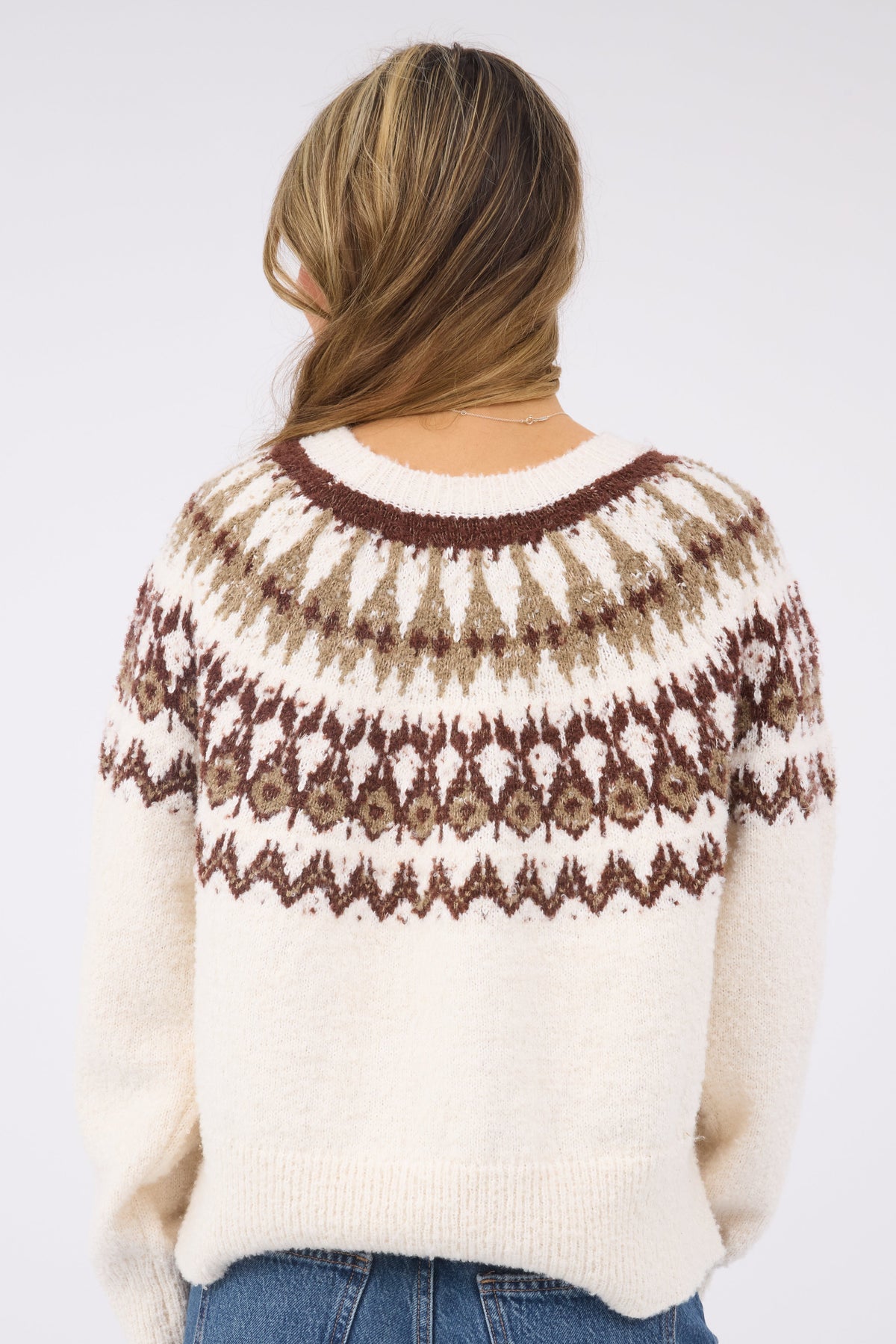 A back view of a woman wearing a cream pullover sweater wtih a brown & beige nordic pattern.