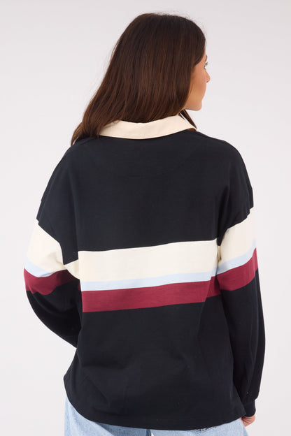 A back view of a woman wearing a black loose fitting top with wide stripe in cream, light blue & maoon. 