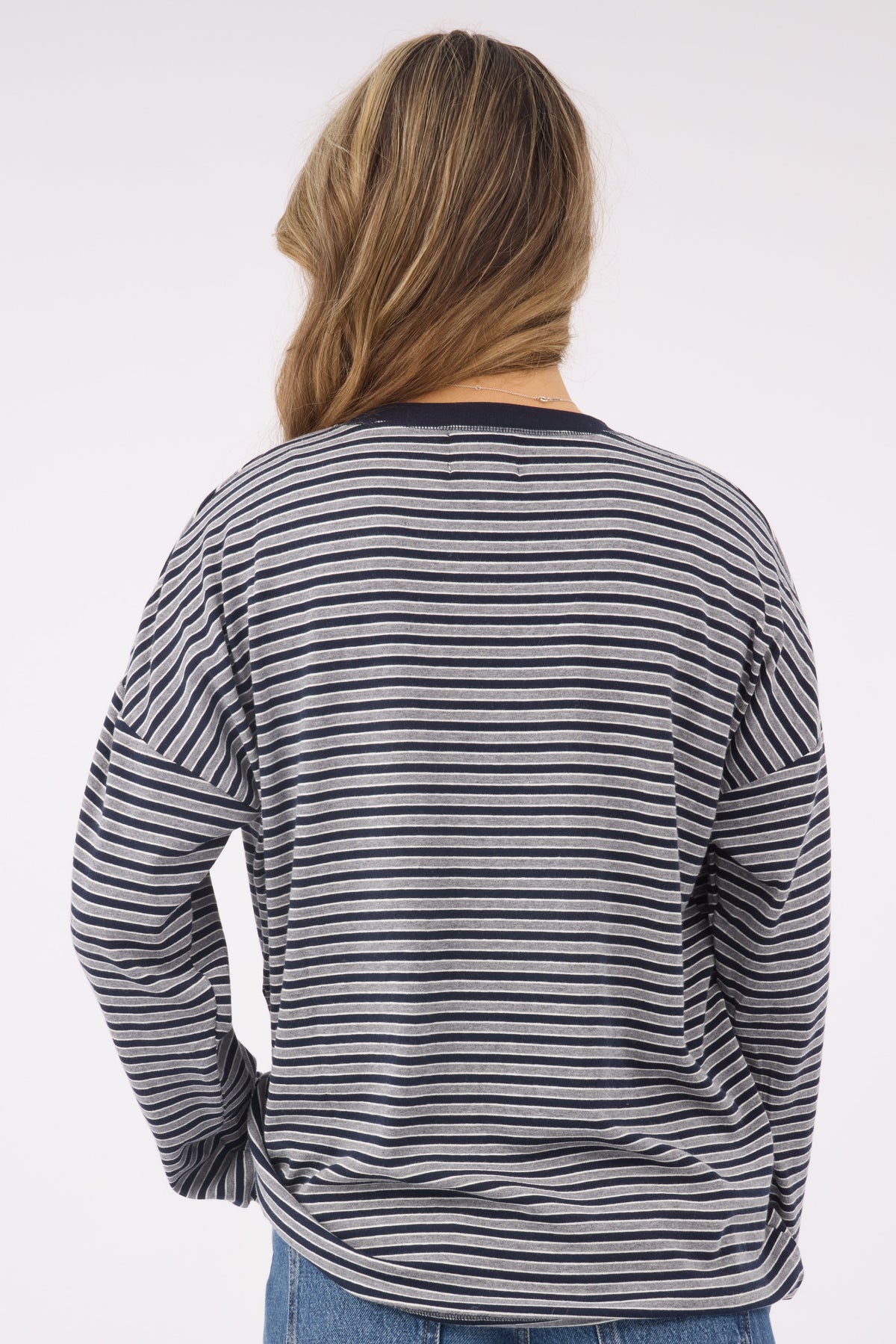 A back view of a woman wearing a loose fitting knit top in navy & grey stripe and long sleeves,