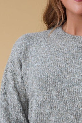 Closer view of a young woman wearing a   light green rib knit sweater with a wide crew neckline.