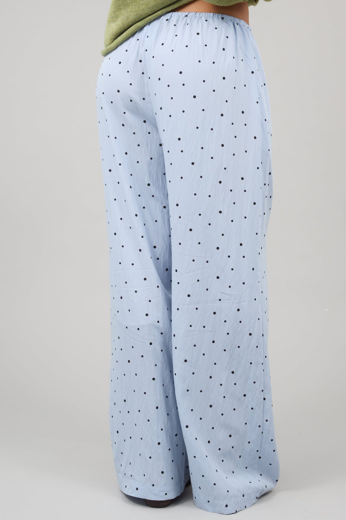 Back view of a woman wearing wide leg blue wide leg pants with black polka dots.