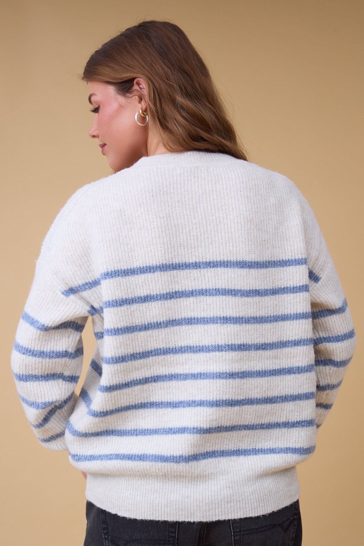 Back view of a woman wearing an oatmeal & blue stripe sweater with long sleeves and a crew neckline.